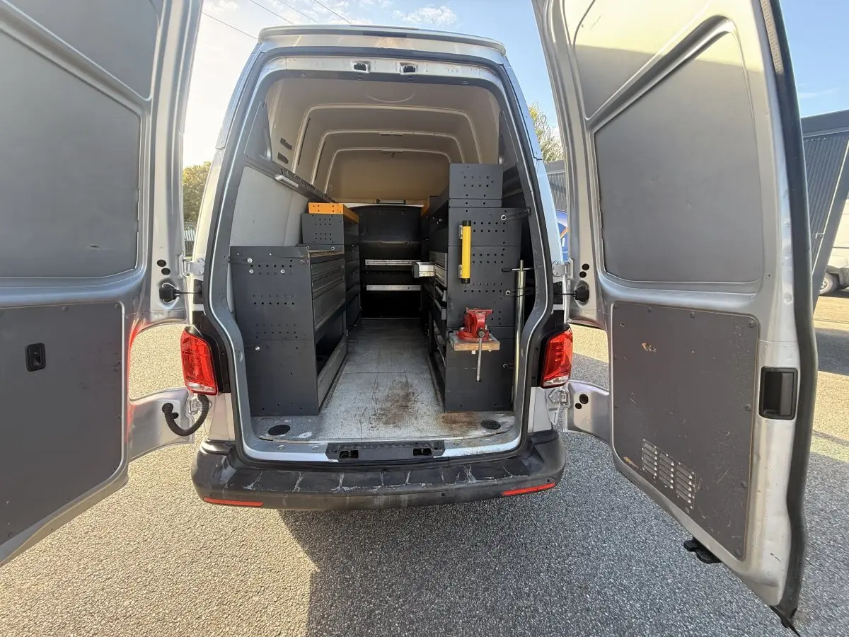 Vue arrière ouverte d’un Volkswagen Transporter gris clair 2022 avec aménagements de rangement noirs dans la zone de chargement.