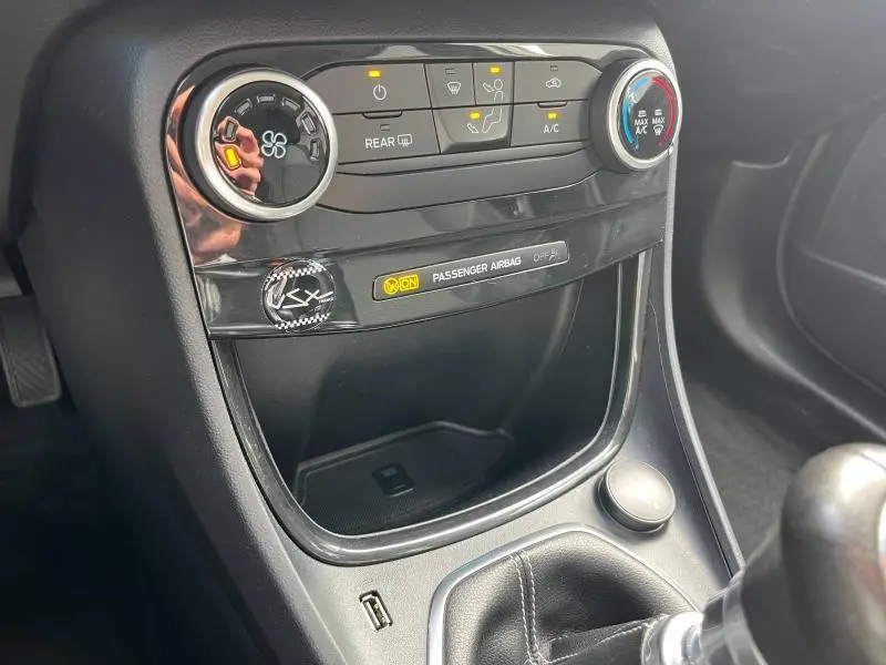 Vue rapprochée de la console centrale noire du Ford Puma 2023 avec commandes climatisation et indicateur airbag passager allumé.