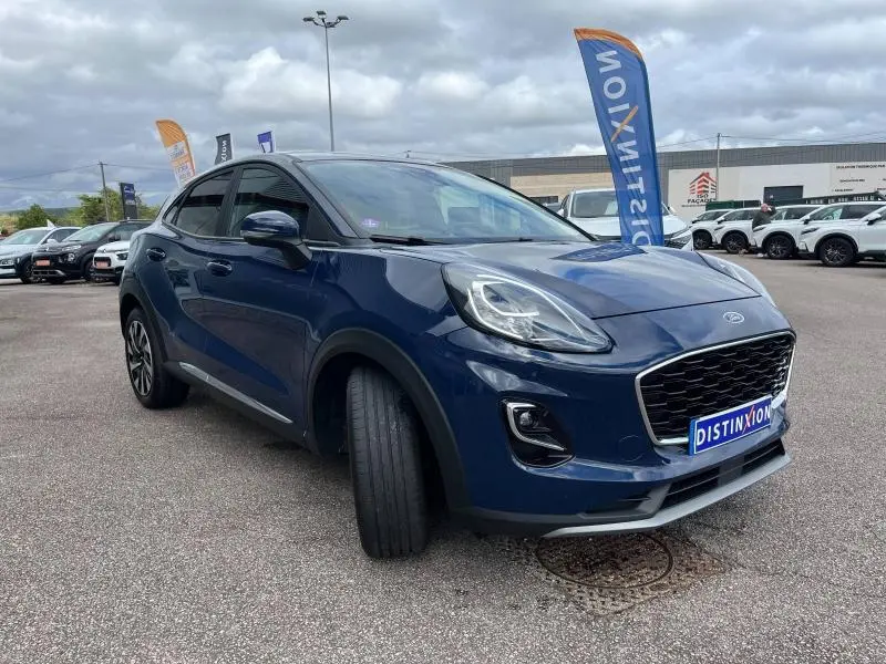 Ford Puma bleu Abysse en vue 3/4 avant droit sur parking avec calandre noire et phares LED distinctifs.