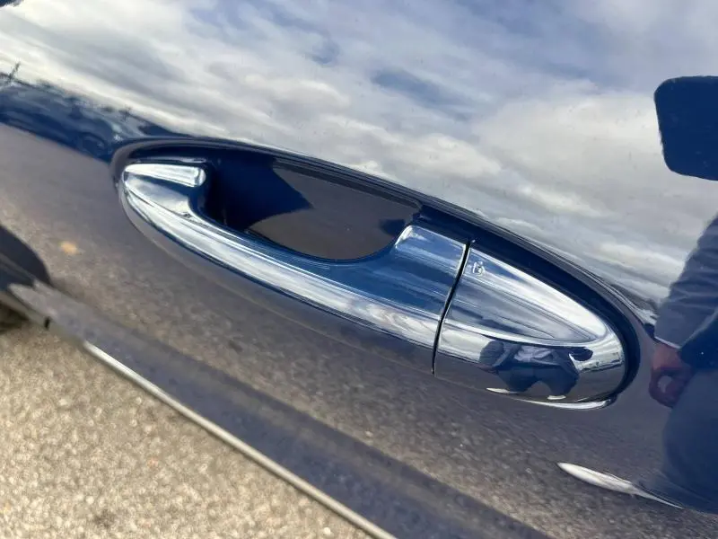 Poignée de porte avant droite chromée sur Ford Puma bleu Abysse 2023, reflet du ciel et d'une personne visible.