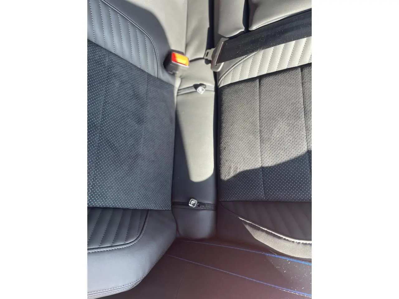 Vue rapprochée des sièges arrière en Alcantara noir avec surpiqûres bleues et ceinture de sécurité visible.