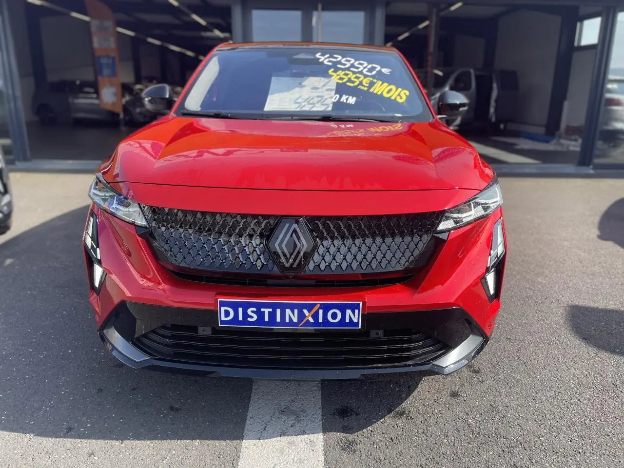 Vue frontale d'une Renault Rafale rouge avec calandre noire et logo distinctif, sur parking extérieur.