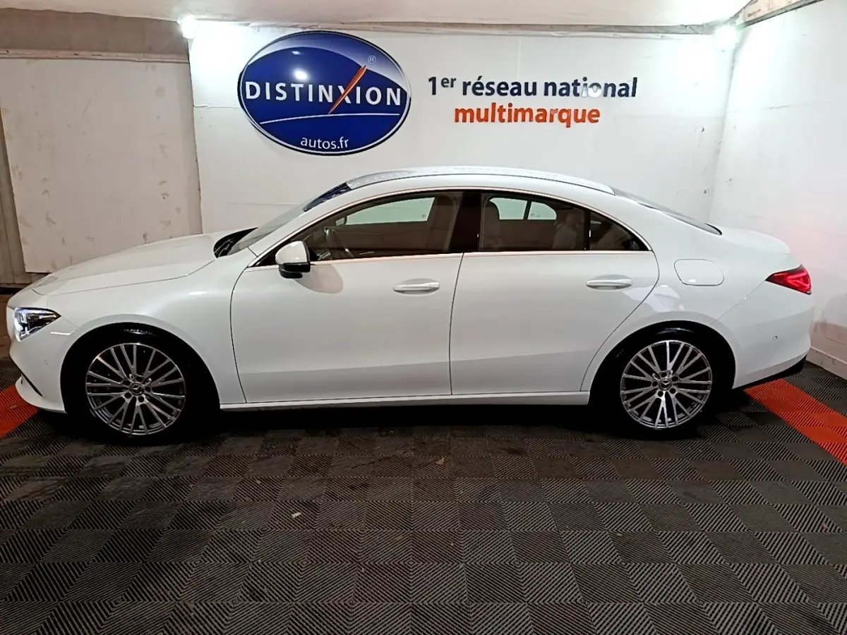 Vue de profil côté gauche d'une Mercedes CLA 200 d Business Line blanche, avec jantes alliage et feux arrière LED allumés.