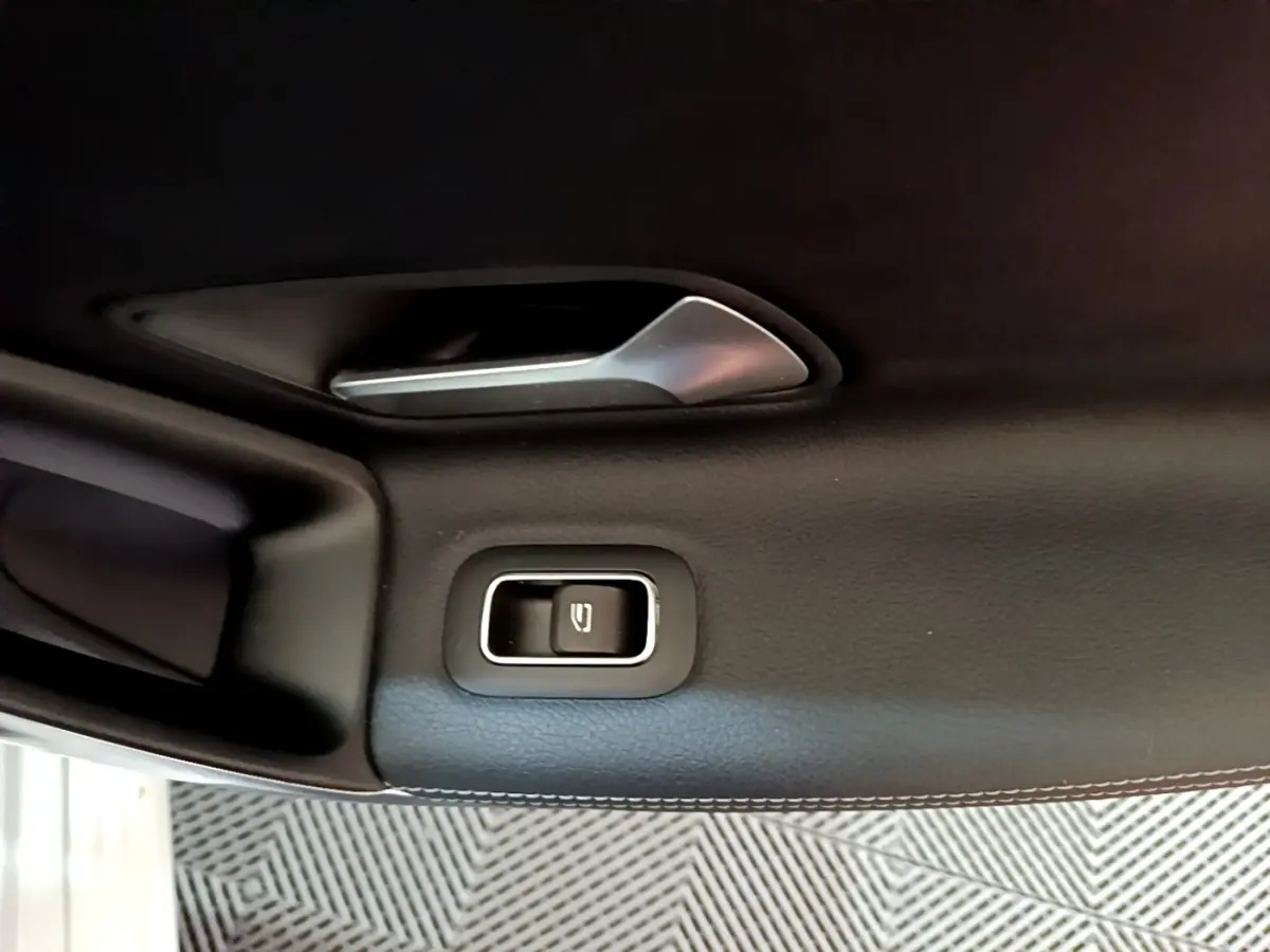 Détail de la poignée intérieure et bouton de verrouillage de porte côté gauche d’une Mercedes CLA 200 d Business Line blanche.