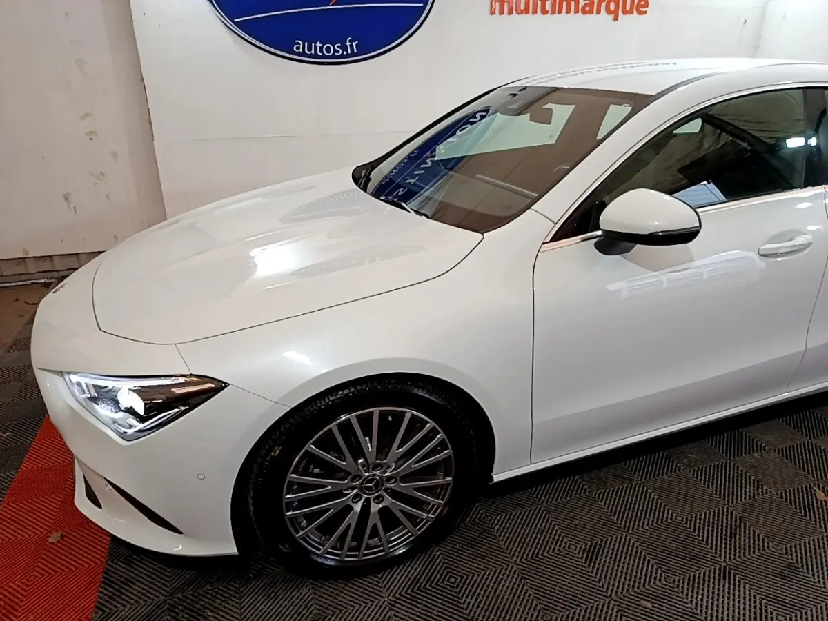 Vue 3/4 avant droit d'une Mercedes CLA 200 d Business Line blanche avec jantes alliage et phares LED allumés.