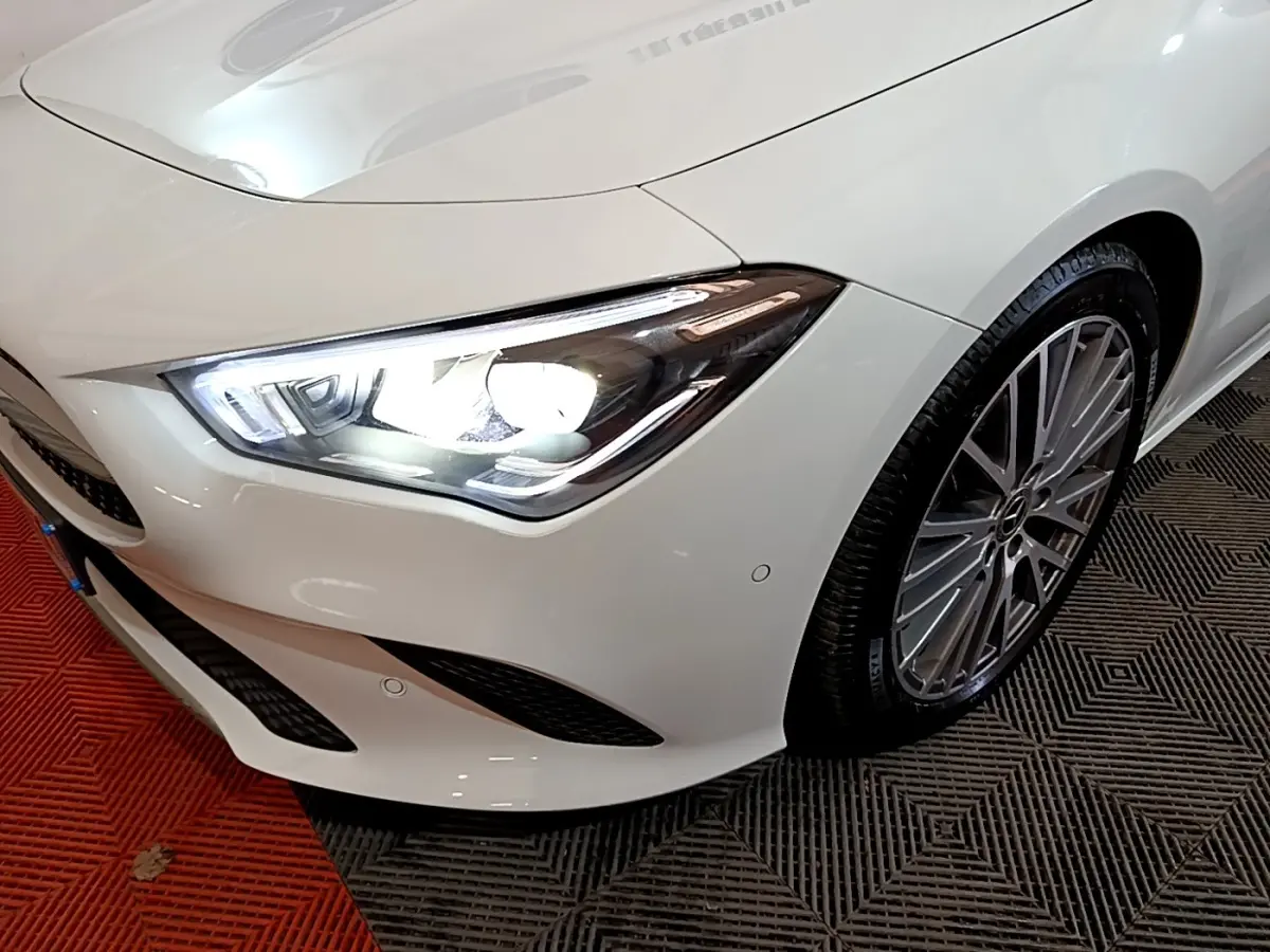 Gros plan sur l’avant droit blanc d’une Mercedes CLA 200 d avec phare LED allumé et jante alliage multibranches.