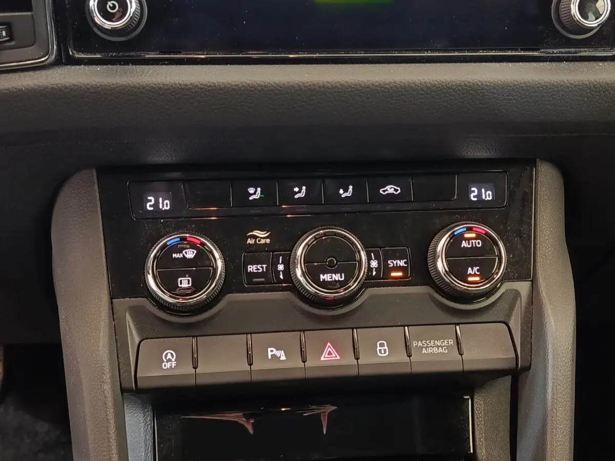 Vue rapprochée du tableau de bord noir du Skoda Kodiaq blanc, montrant les commandes de climatisation digitale et les boutons fonctionnels.