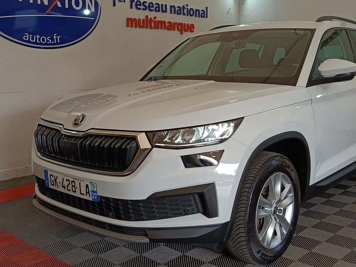 Vue 3/4 avant d'un Skoda Kodiaq blanc 2022 avec calandre noire et phares LED dans un showroom.
