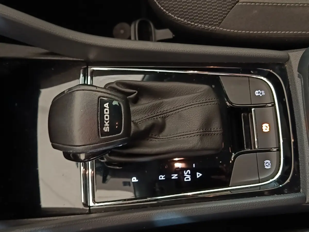 Gros plan sur la commande de boîte automatique noire avec logo ŠKODA, entourée de boutons de contrôle éclairés.