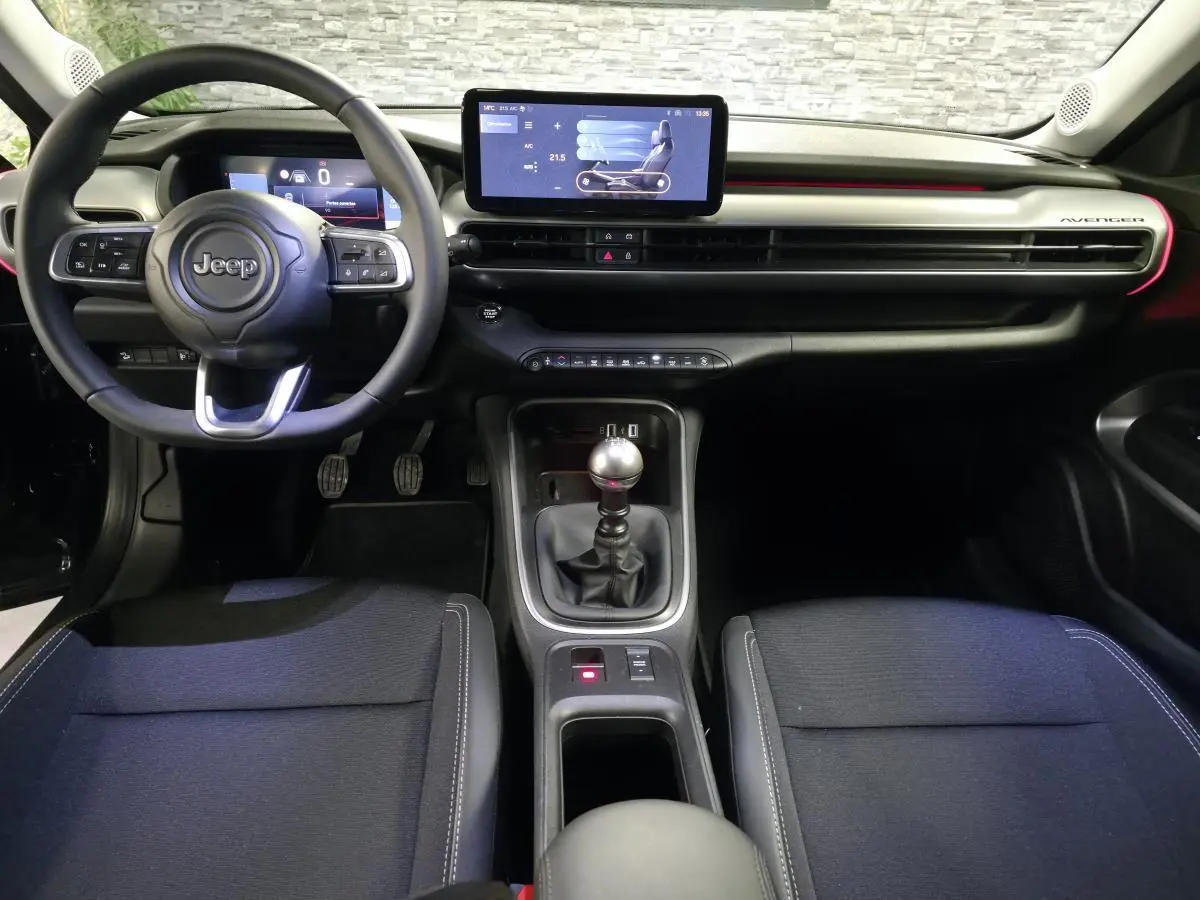 Vue intérieure avant du Jeep Avenger 2025 noir, volant multifonction, écran tactile central et levier de vitesses manuel.