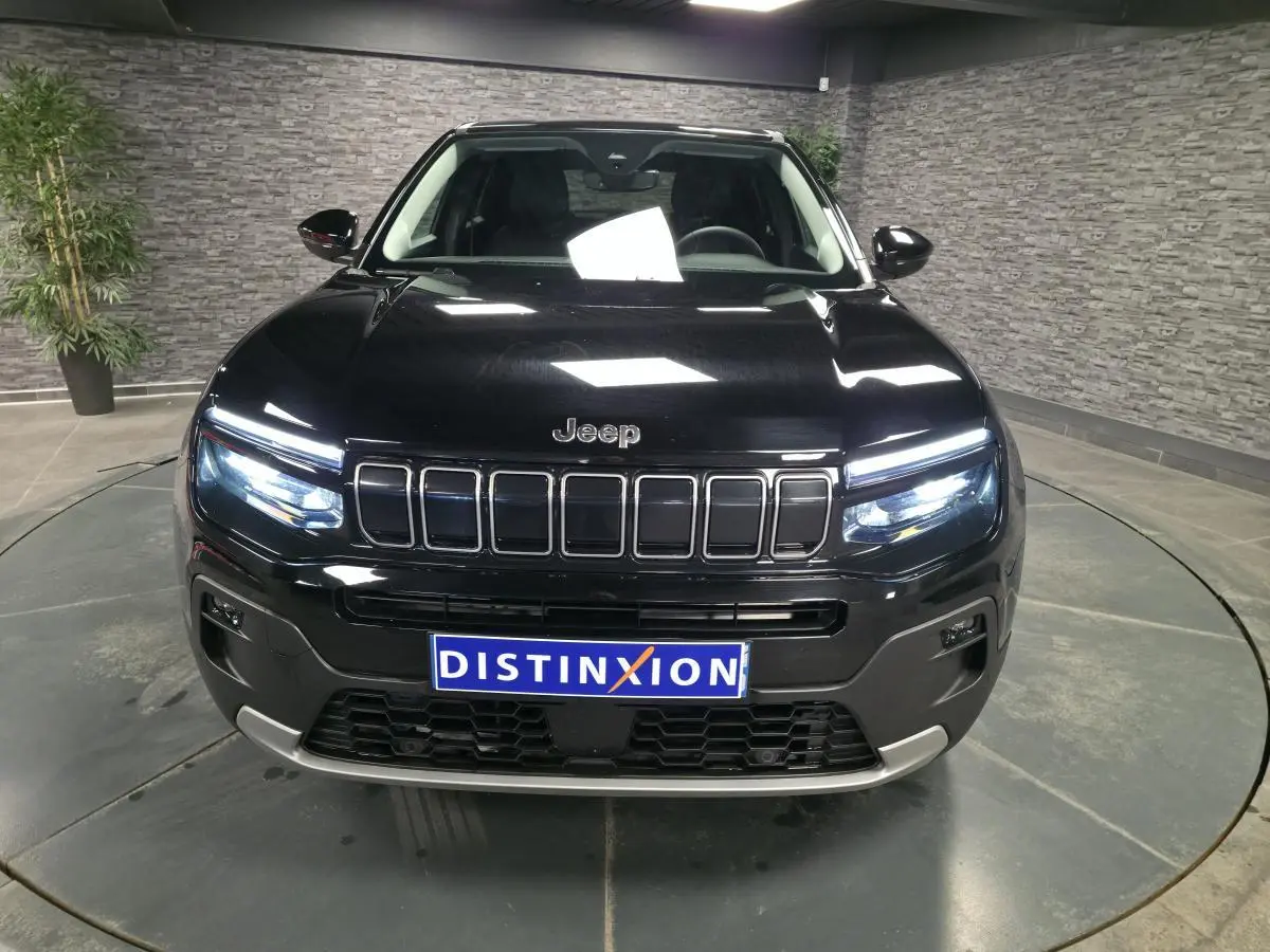 Vue frontale du Jeep Avenger noir 2025 avec calandre gloss black et phares LED allumés dans un showroom.