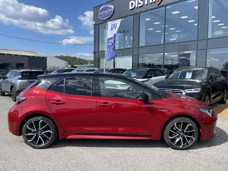 Vue de profil côté gauche d'une Toyota Corolla 184 H Collection rouge métal avec toit noir, roues alliage et vitres teintées.