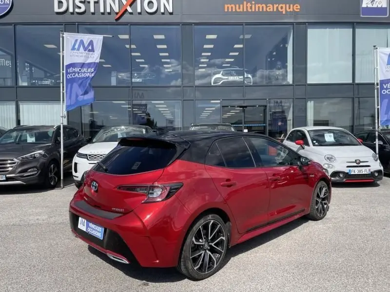 Toyota Corolla 184 H Collection rouge métal avec toit noir, vue 3/4 arrière droit sur parking de concession.