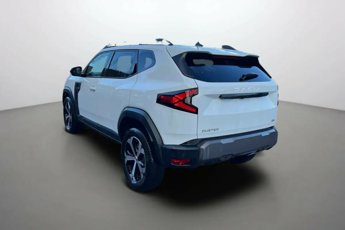 Vue 3/4 arrière du Dacia Duster blanc glacier 2025 avec jantes alliage et feux arrière en forme de flèche.