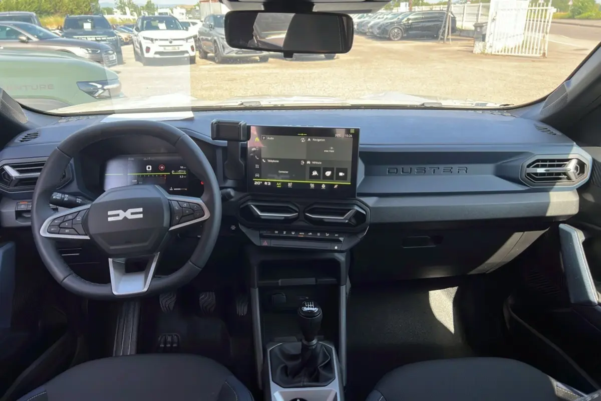 Intérieur du Dacia Duster 2025 blanc glacier, vue frontale sur le tableau de bord avec écran tactile et volant multifonction.