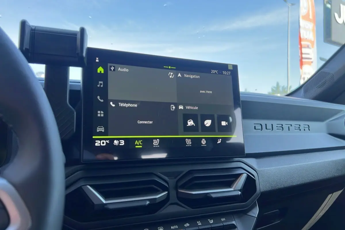 Tableau de bord du Dacia Duster 2025 blanc glacier, vue intérieure centrée sur l'écran tactile et les aérateurs hexagonaux.