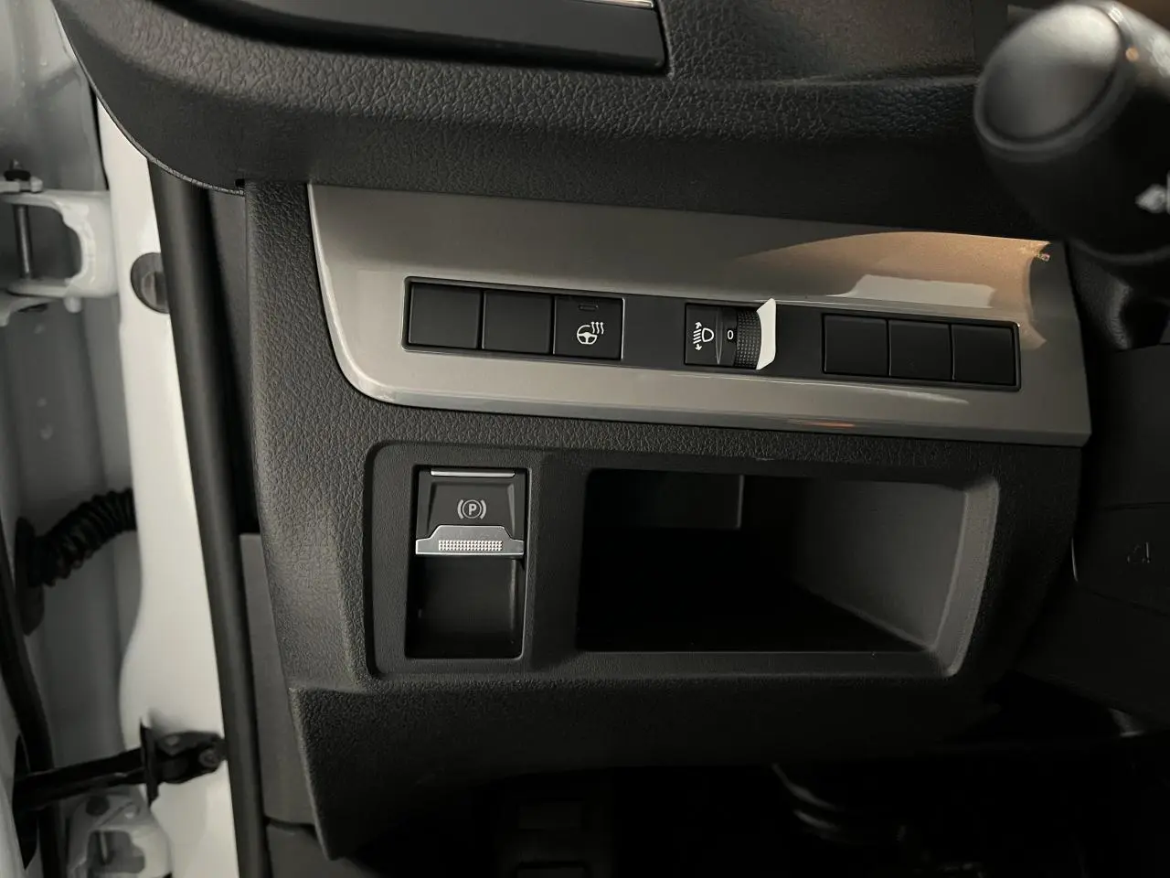 Détail de la console côté gauche du tableau de bord du Peugeot Expert Fourgon blanc 2024 avec commandes du frein de stationnement et réglage des phares.
