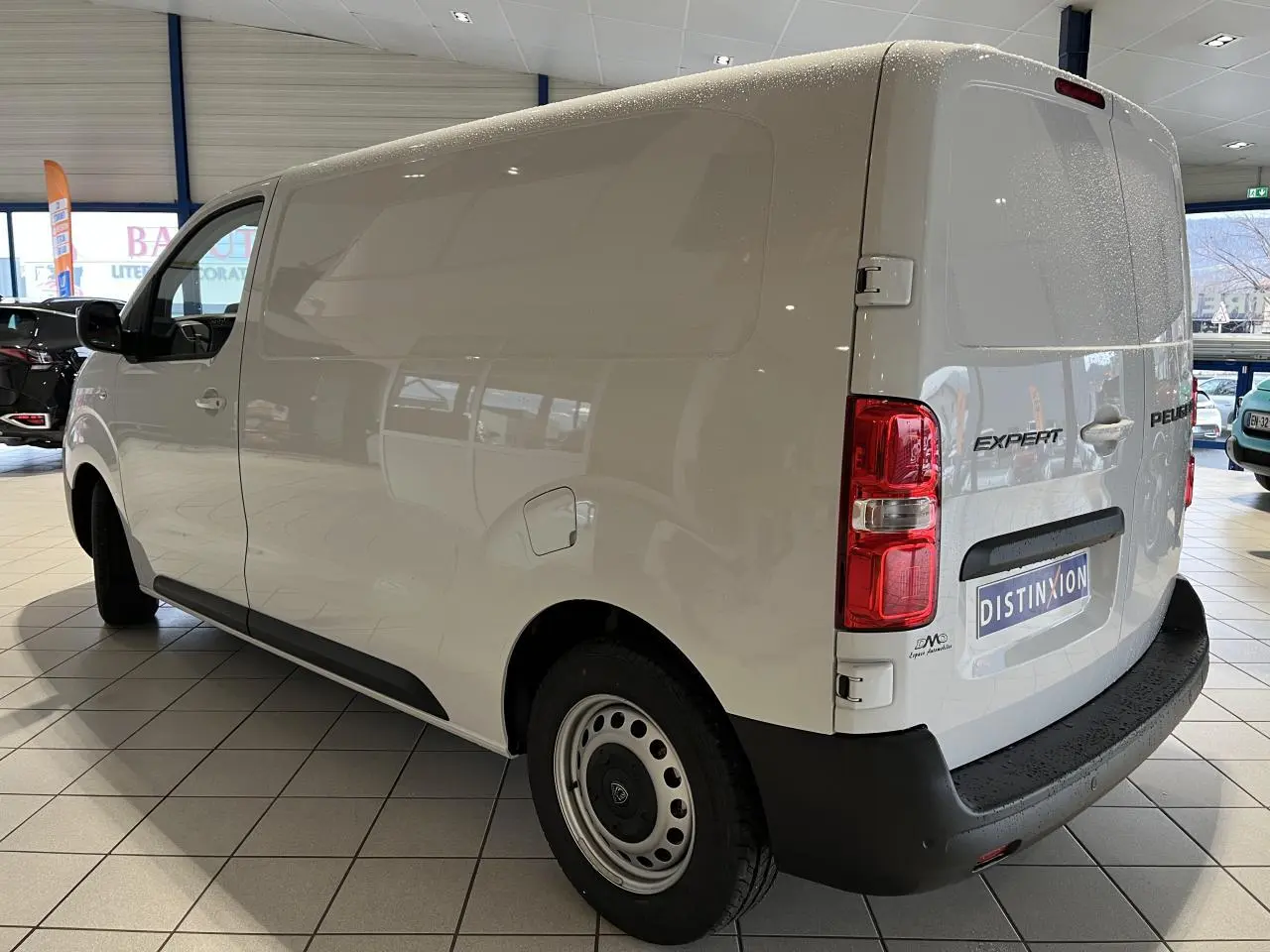 Vue 3/4 arrière droite du Peugeot Expert Fourgon blanc avec roues tôles grises et pare-chocs noirs en intérieur showroom.