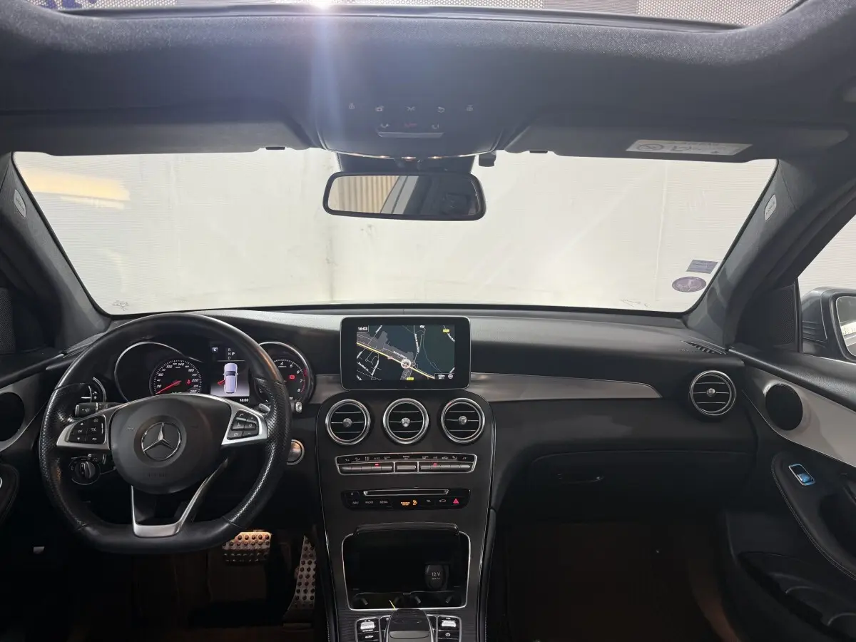 Vue intérieure avant du tableau de bord noir d'une Mercedes GLC 250 Fascination 4Matic avec écran central et volant cuir.