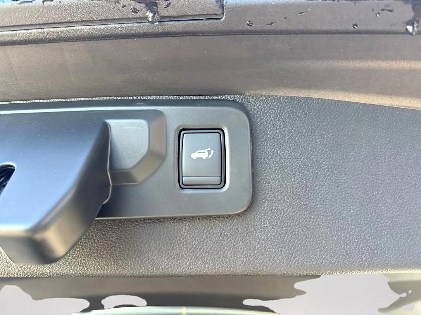 Gros plan sur le bouton d'ouverture électrique du coffre dans le coffre d'une Renault Symbioz gris rafale.