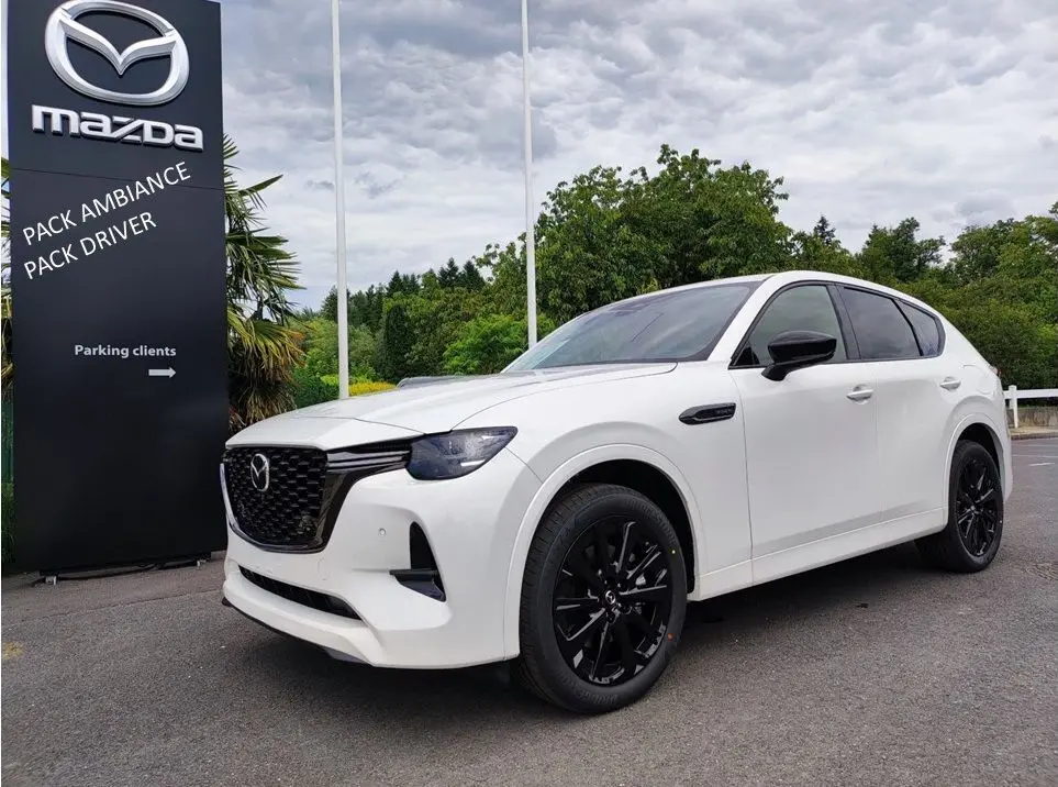 Vue 3/4 avant droite d'un Mazda CX-60 blanc métal avec jantes noires et vitres teintées, devant un panneau Mazda.
