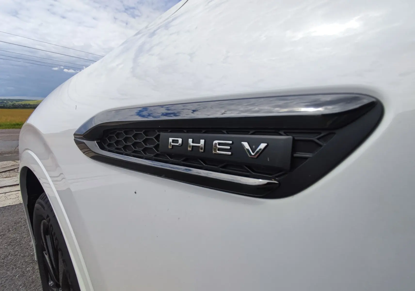 Gros plan sur l'aile avant gauche blanche métallisée du Mazda CX-60 avec l'emblème PHEV noir brillant.