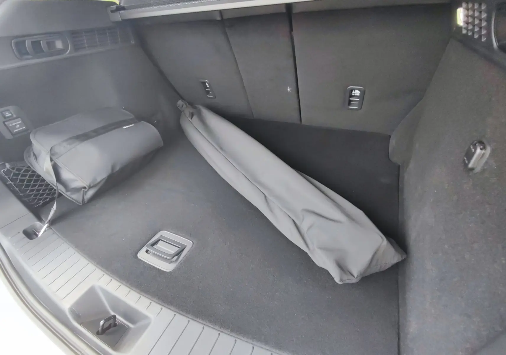 Vue intérieure du coffre noir du Mazda CX-60 2024 avec sac et housse d'accessoires posés au sol.