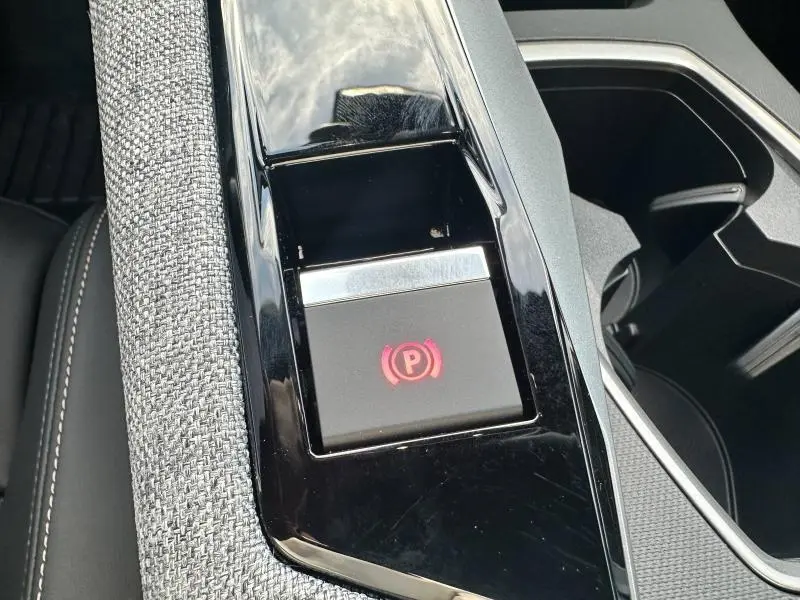 Gros plan sur le bouton de frein de stationnement électrique rouge, entouré de garniture noire et tissu gris dans le Peugeot 3008 noir.