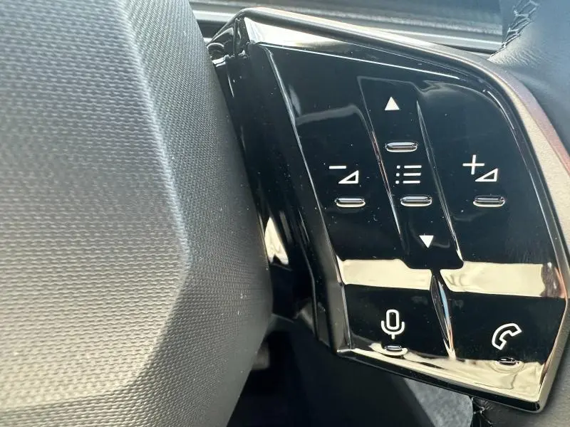 Gros plan sur les commandes au volant noir brillant du Peugeot 3008 Hybrid 2025, avec touches de volume et appel.