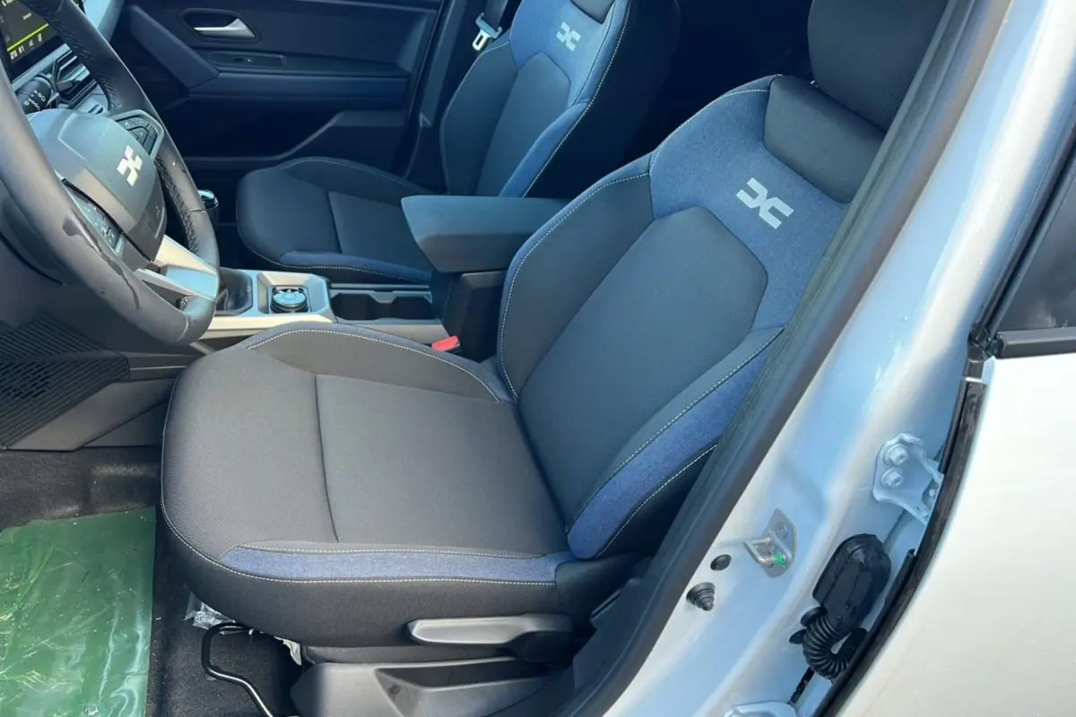 Vue intérieure côté conducteur du Dacia Duster 2025 blanc glacier, sièges tissu noir et bleu avec logo distinctif brodé.