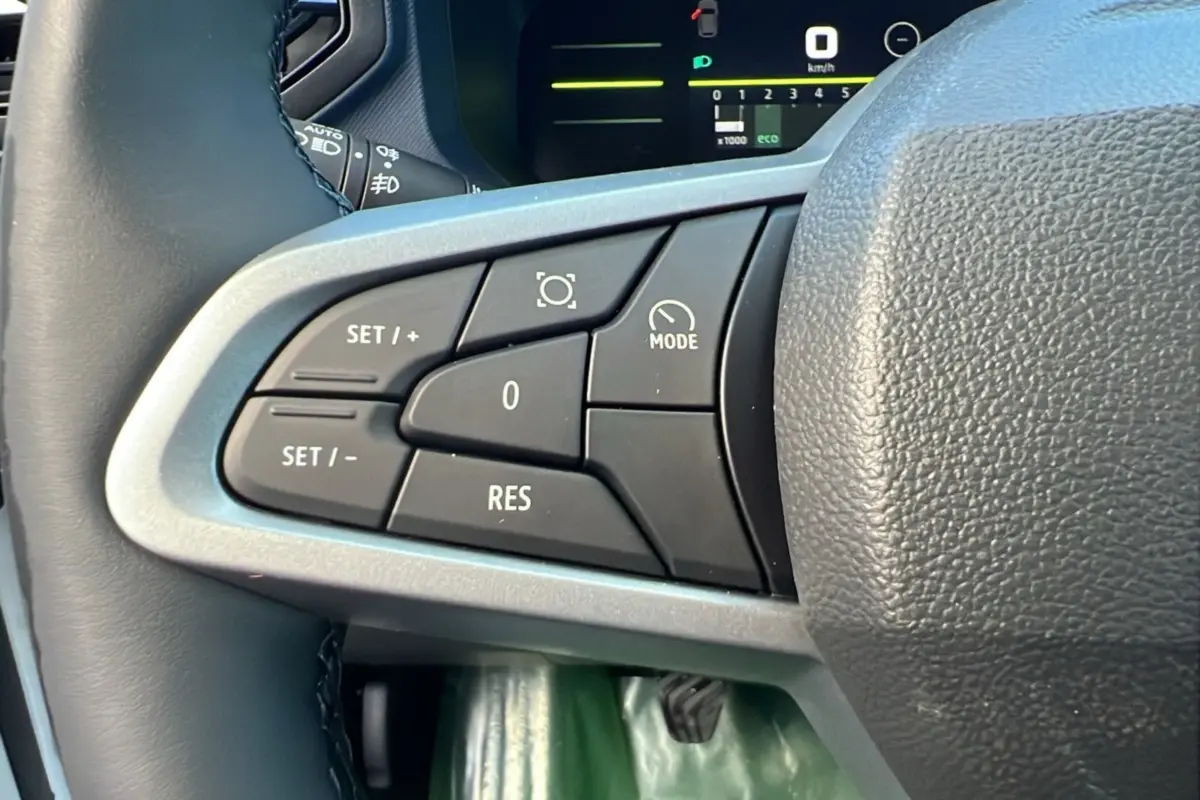 Gros plan sur les commandes au volant côté gauche du Dacia Duster blanc glacier 2025, version NEW TCE 130 4X4 JOURNEY PLUS.