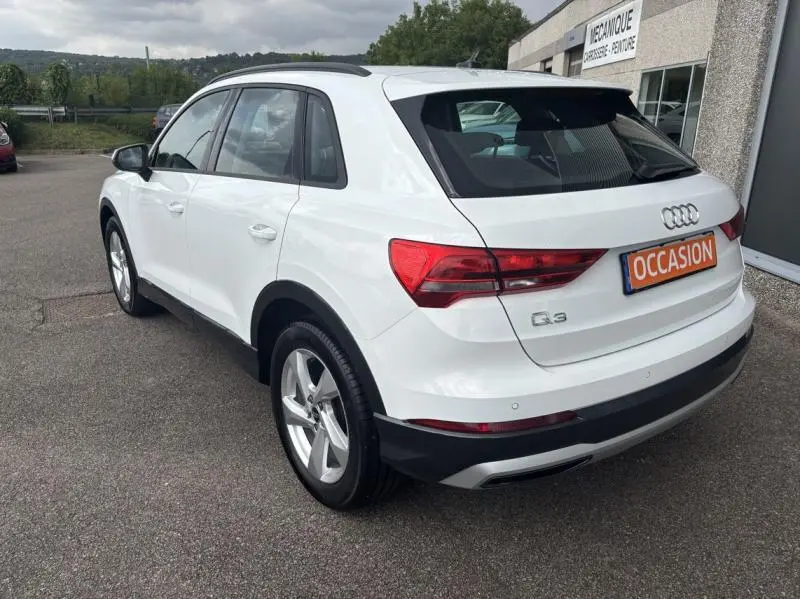 Audi Q3 blanc Glacier métallisé vue 3/4 arrière droit avec feux LED et plaque occasion sur parking.