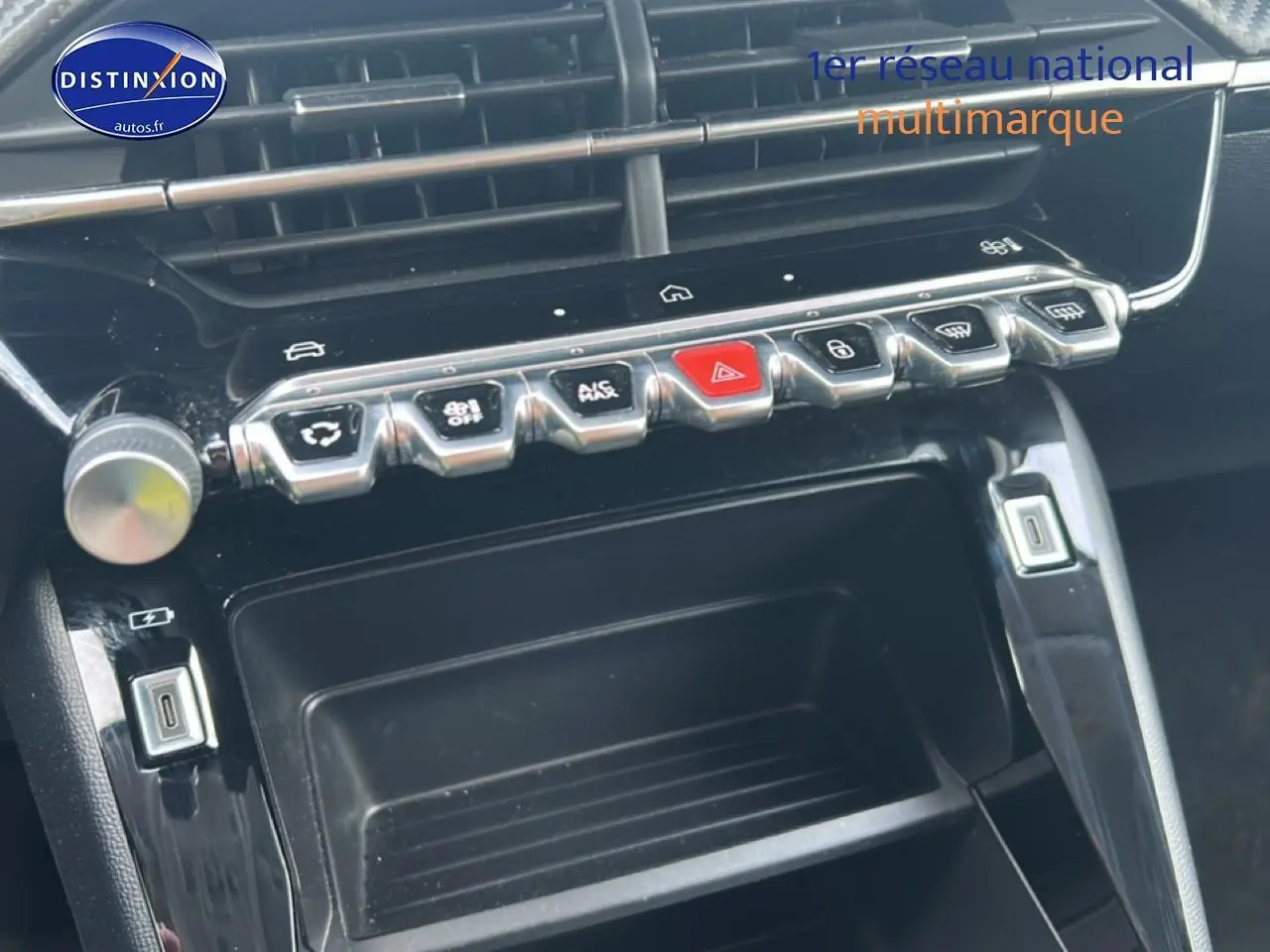 Gros plan sur la console centrale noire brillante de la Peugeot 208 1.2 100 style avec rangements et boutons chromés.