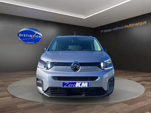 Vue frontale d'un Citroën Berlingo gris Artense avec calandre noire et logo central, en showroom intérieur.