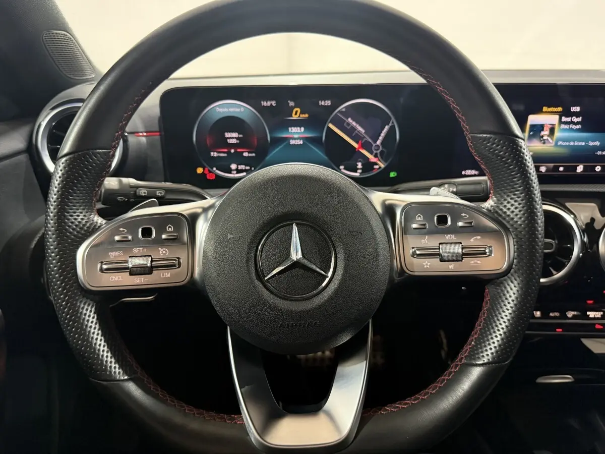 Vue rapprochée du volant cuir noir avec surpiqûres rouges et tableau de bord numérique de la Mercedes Classe A AMG Line 2021.