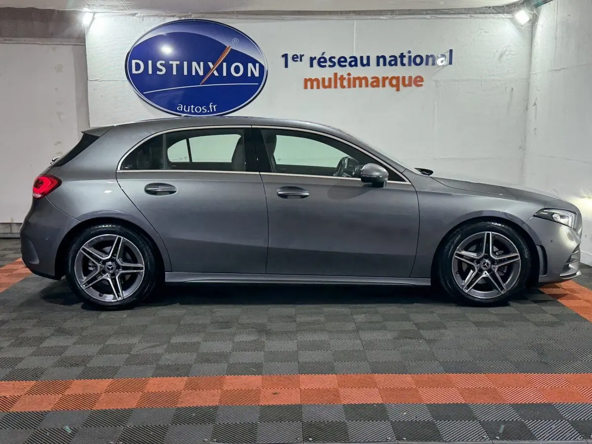 Vue latérale droite d'une Mercedes Classe A 200 AMG Line gris foncé, avec jantes alliage et feux arrière LED allumés.