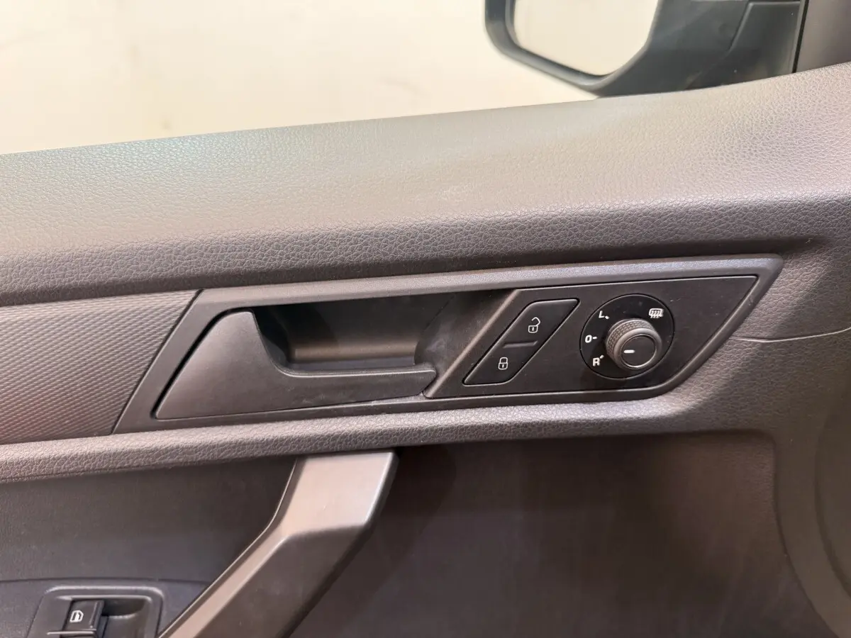 Détail de la poignée intérieure côté conducteur du Volkswagen Caddy noir avec commandes de verrouillage et réglage des rétroviseurs.