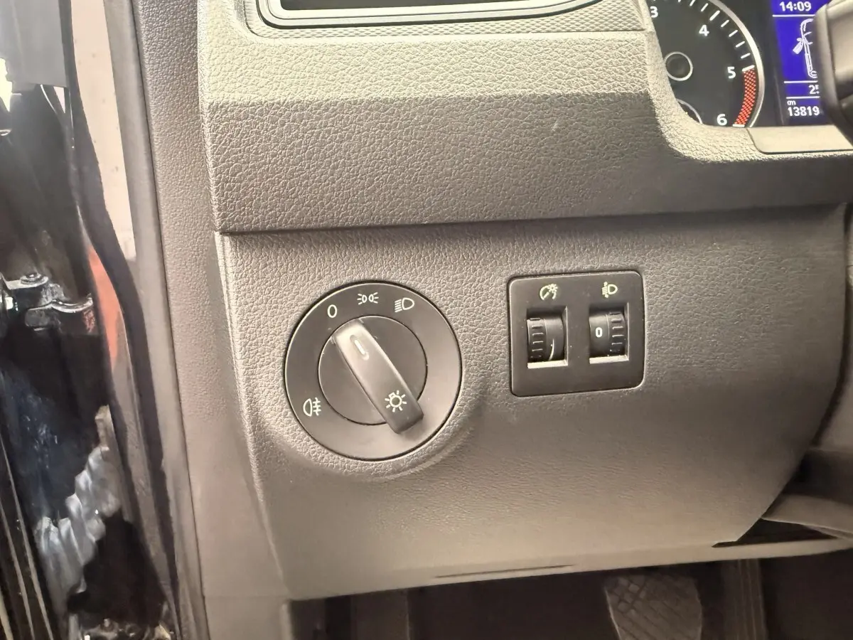 Détail du tableau de bord côté gauche du Volkswagen Caddy noir 2019, avec commandes des phares et réglages lumineux.