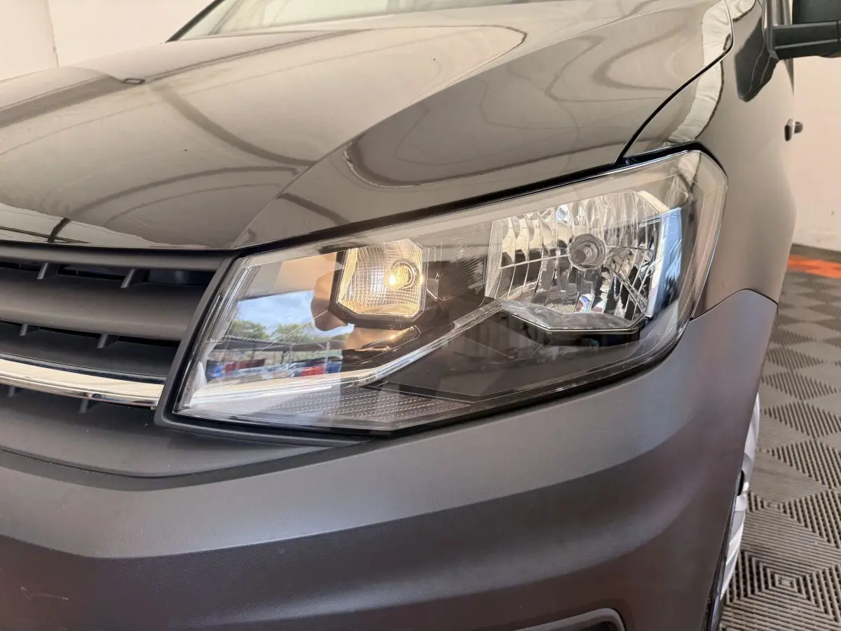 Gros plan sur le phare avant droit du Volkswagen Caddy noir, avec calandre et partie du capot visibles.