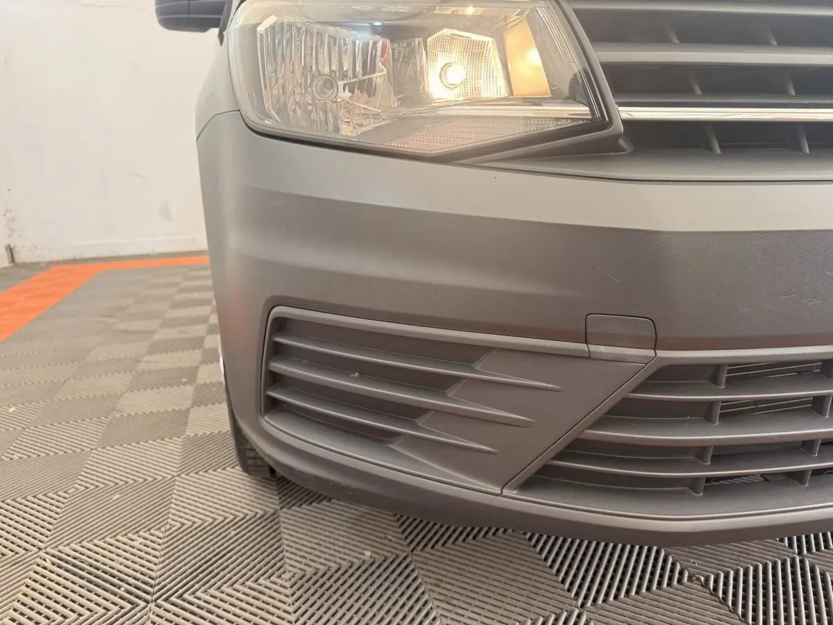 Gros plan sur l'avant gauche noir du Volkswagen Caddy 2.0 TDI 2019 avec phare allumé et calandre visible.