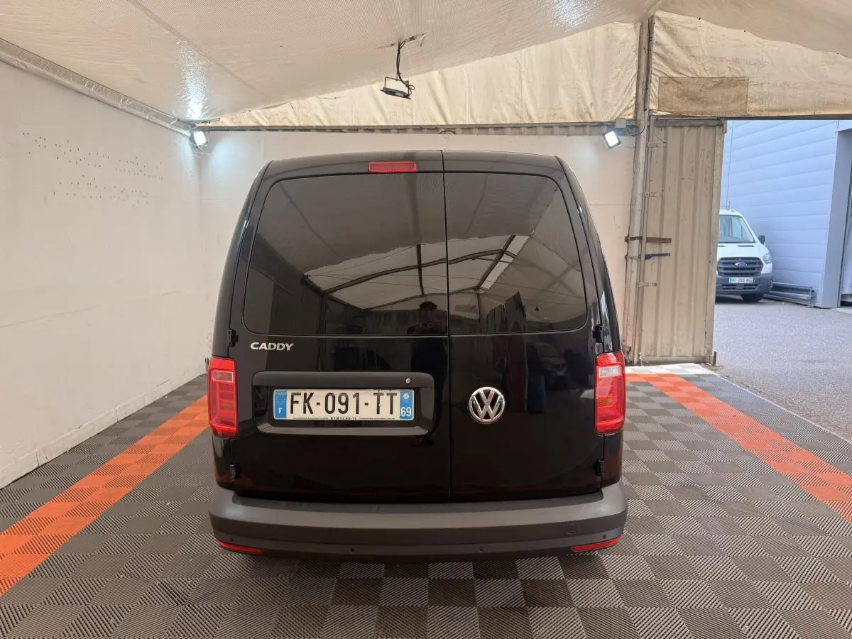 Vue arrière d'un Volkswagen Caddy noir 2019, portes battantes fermées dans un espace couvert avec sol à damier.
