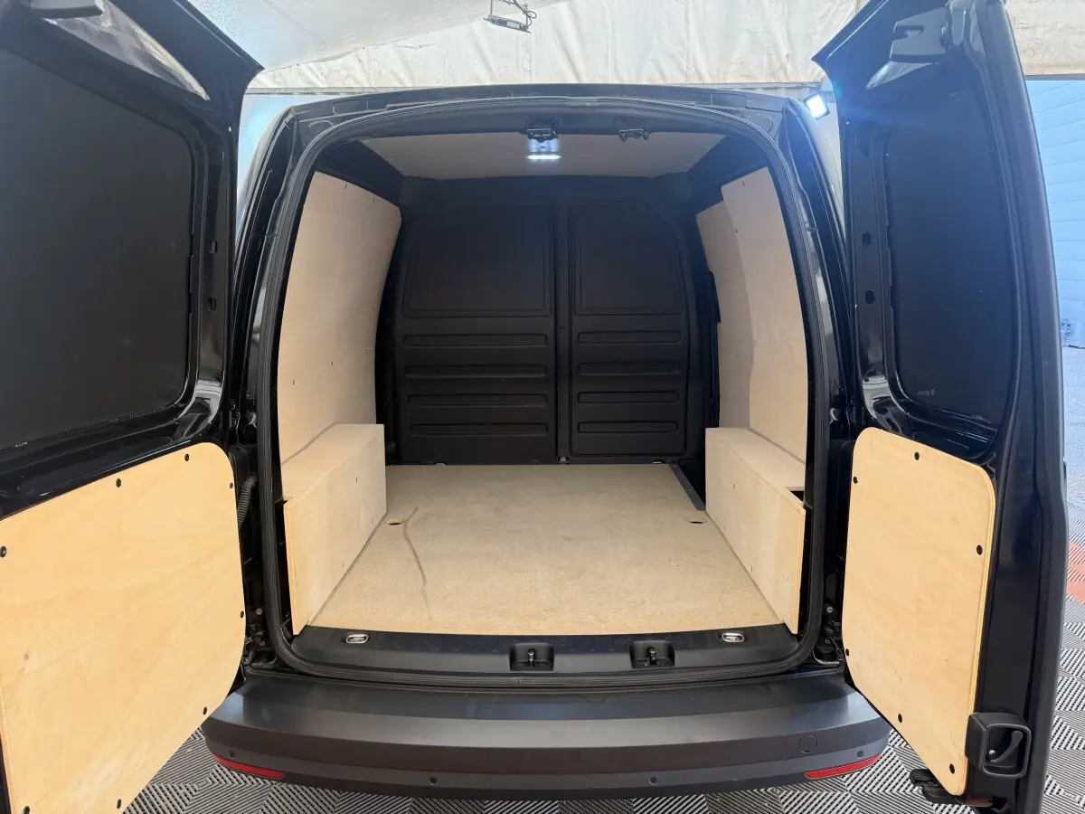 Vue arrière du Volkswagen Caddy noir 2019, montrant l'espace de chargement vide avec habillage bois clair.
