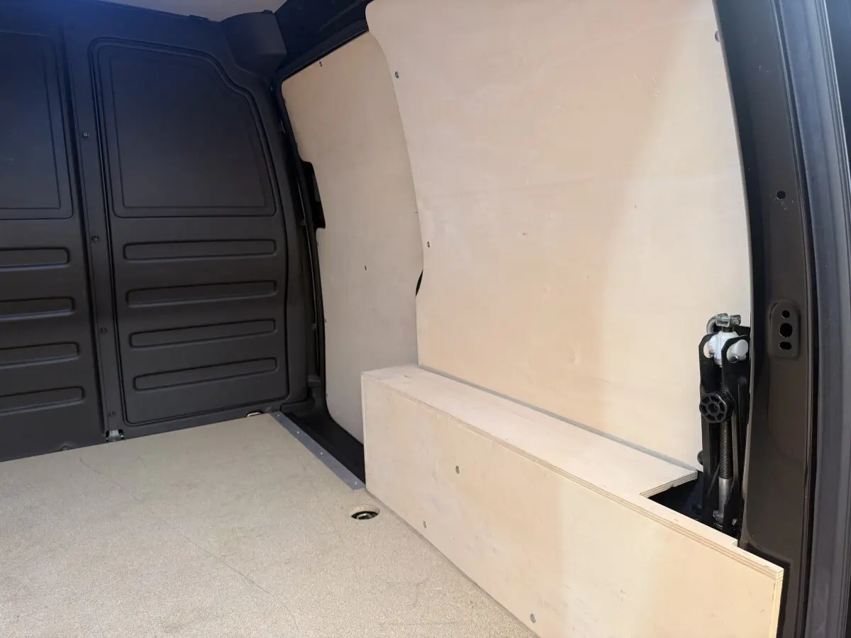 Intérieur du coffre d’un Volkswagen Caddy noir, vue latérale droite montrant la cloison et le plancher en bois clair.