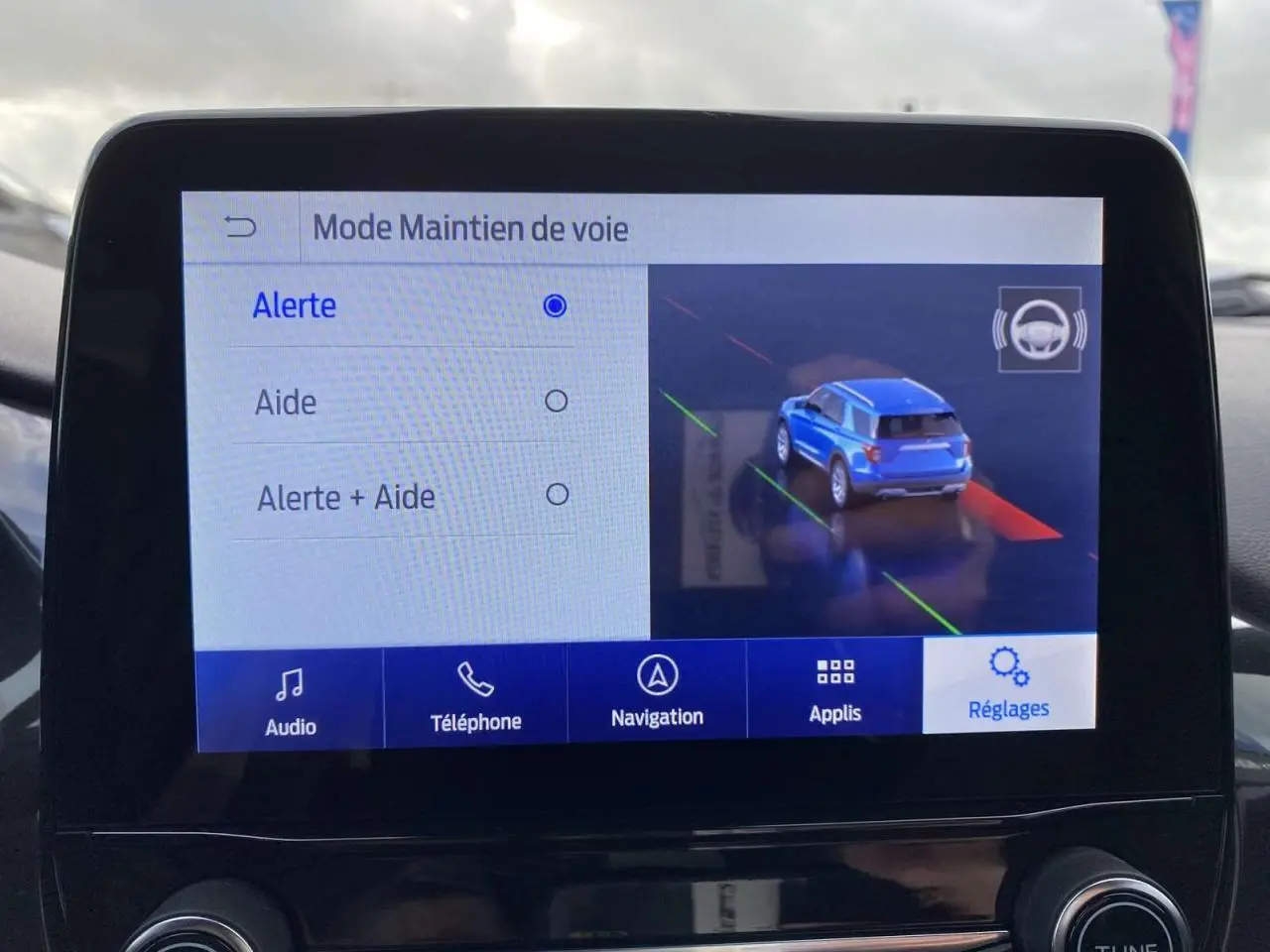 Écran tactile intérieur montrant le mode maintien de voie avec une voiture bleue en vue arrière sur l'affichage.