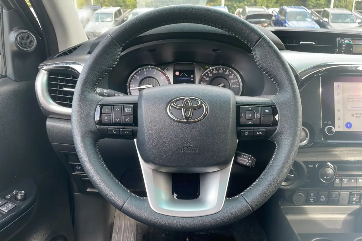 Vue centrée sur le volant noir du Toyota Hilux 2025, avec tableau de bord et commandes visibles en arrière-plan.