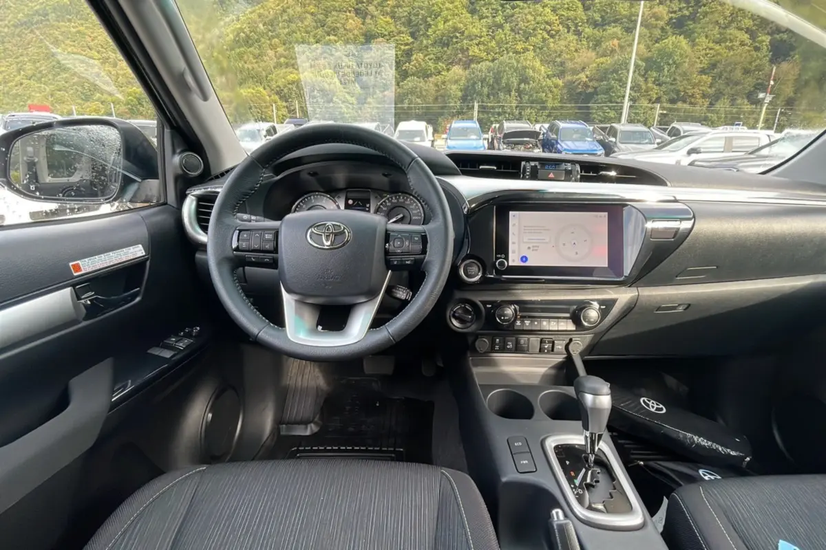 Vue intérieure du tableau de bord et volant du Toyota Hilux 4x4 2025, avec écran tactile et levier de vitesses automatique.
