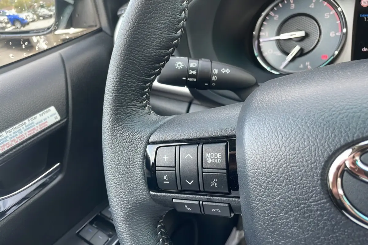 Gros plan sur les commandes au volant à gauche d'un Toyota Hilux 2025, finition Bronze Imperial, avec tableau de bord en arrière-plan.