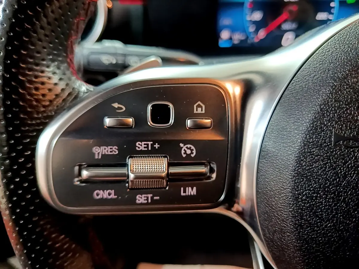 Gros plan sur les commandes du régulateur de vitesse au volant cuir perforé d’une Mercedes Classe A noir 2021.