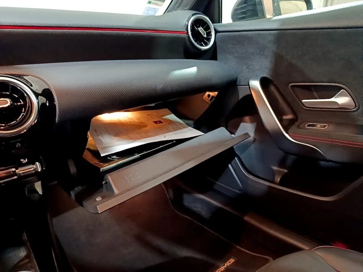 Intérieur noir de la Mercedes Classe A 200 AMG Line 2021, vue côté passager avec boîte à gants ouverte et détails rouges.