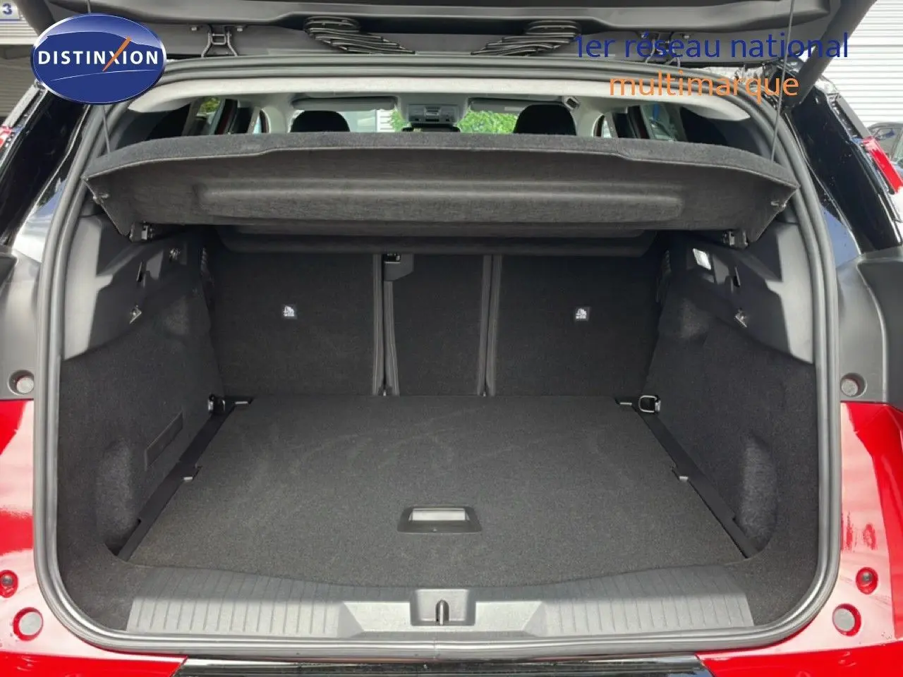Coffre ouvert vu de l'arrière d'un Citroën C5 Aircross Hybrid rouge rubis, montrant l'espace de chargement vide.
